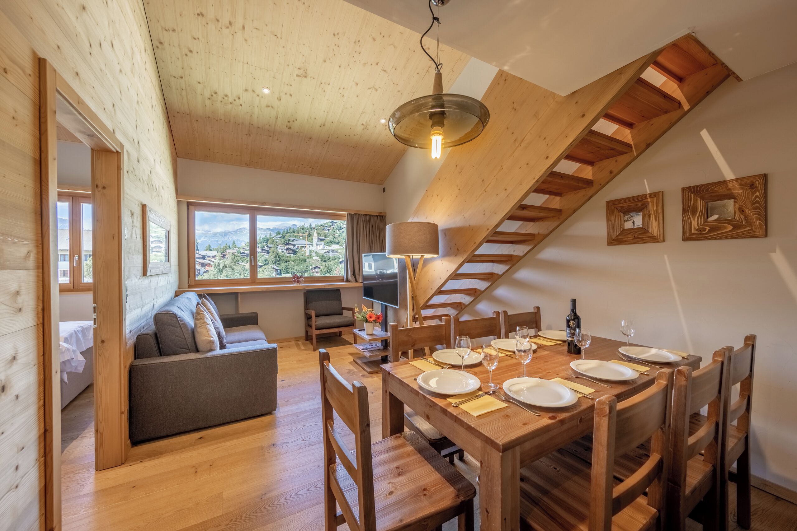 Un intérieur en bois comprenant une table à manger pour quatre personnes, un canapé, un téléviseur et un escalier.
