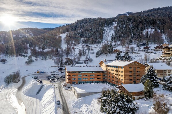A snow-covered mountain resort with wooden buildings, a ski slope, and a parking area. - SWISSPEAK Resorts by Pierre & Vacances Premium Vercorin (Chalais)