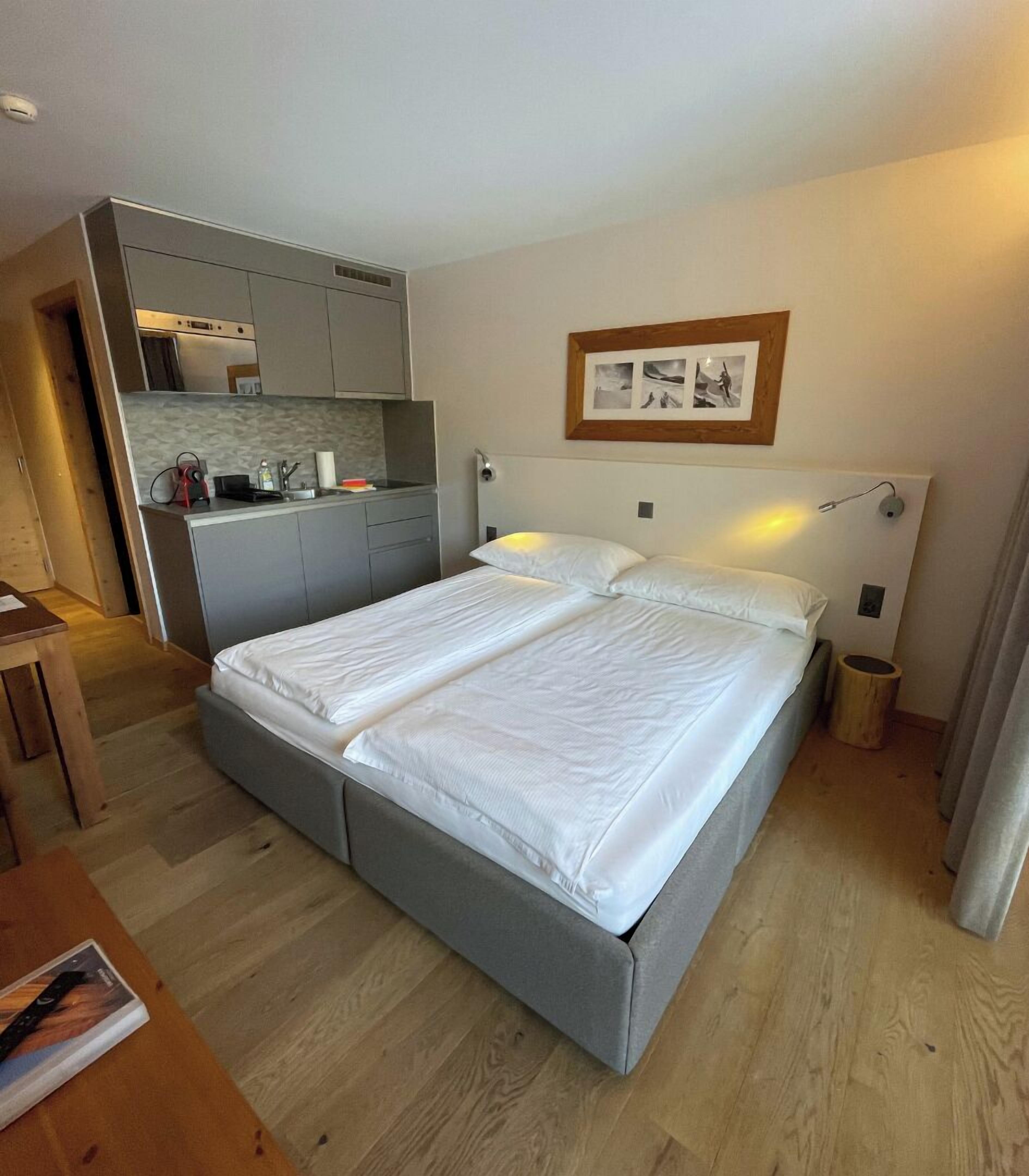 A bedroom with a double bed, a small kitchenette, and a wooden floor.