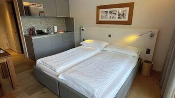 A bedroom with a double bed, a small kitchenette, and a wooden floor.
