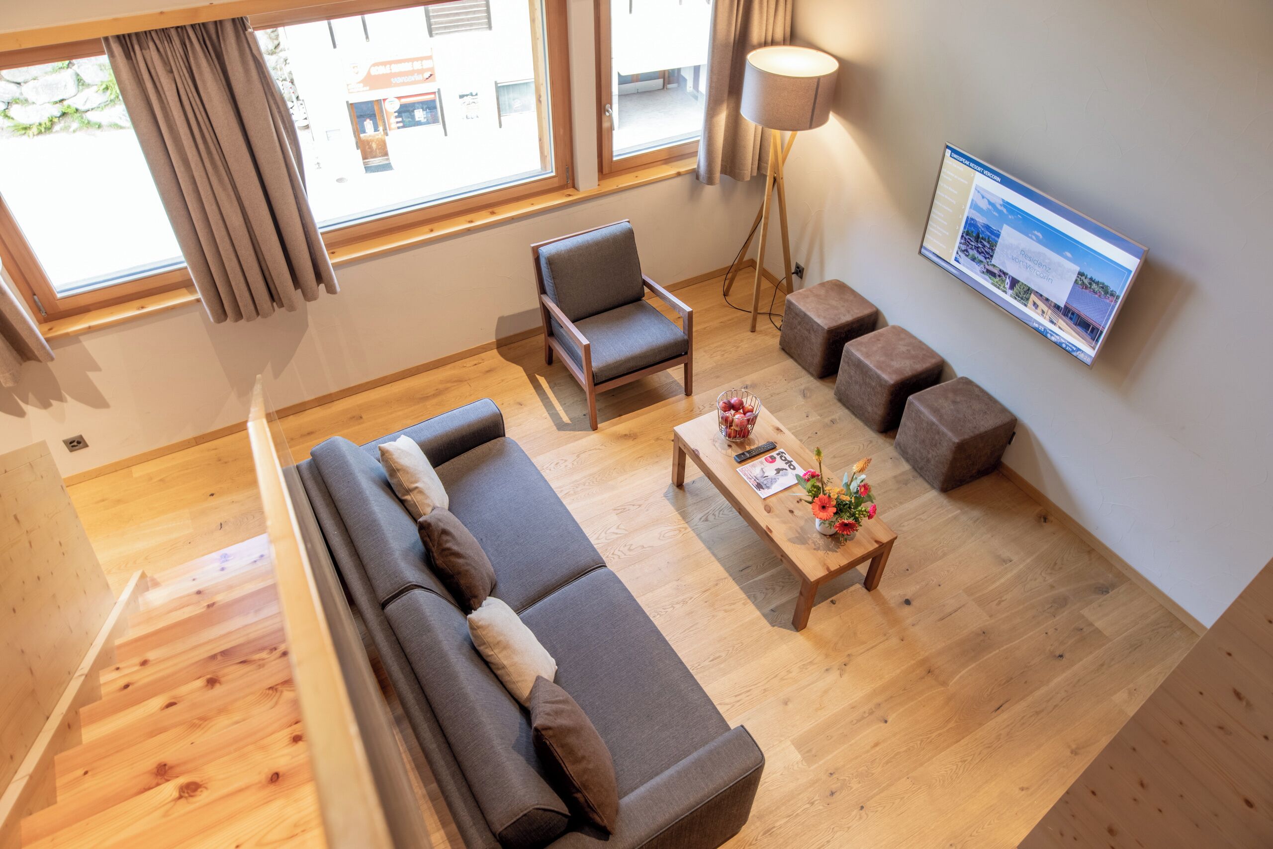 A modern living room with a sofa, armchair, coffee table, and a flat-screen TV mounted on the wall.
