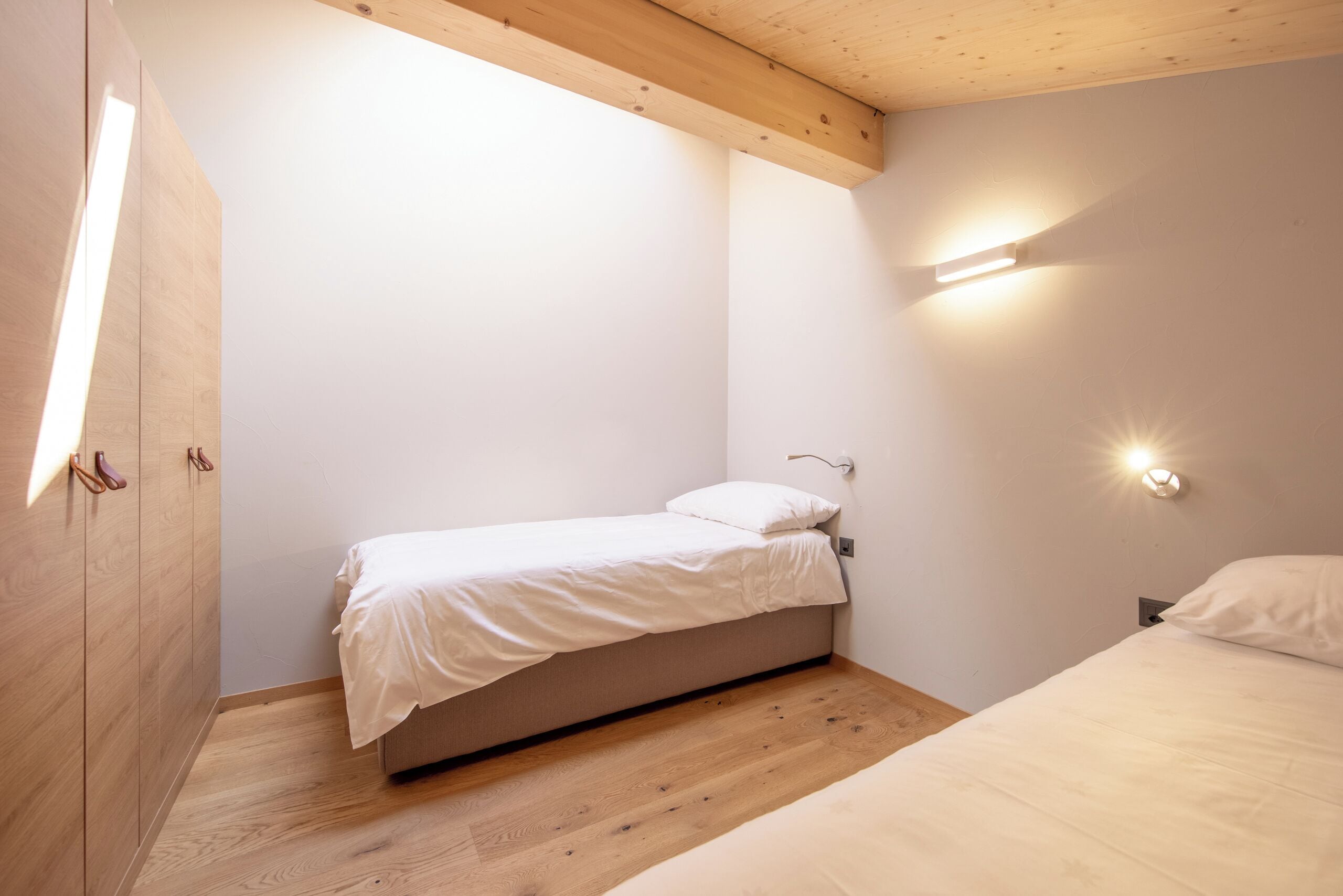 A bedroom with a single bed, a wooden wardrobe, and a wall-mounted light fixture.