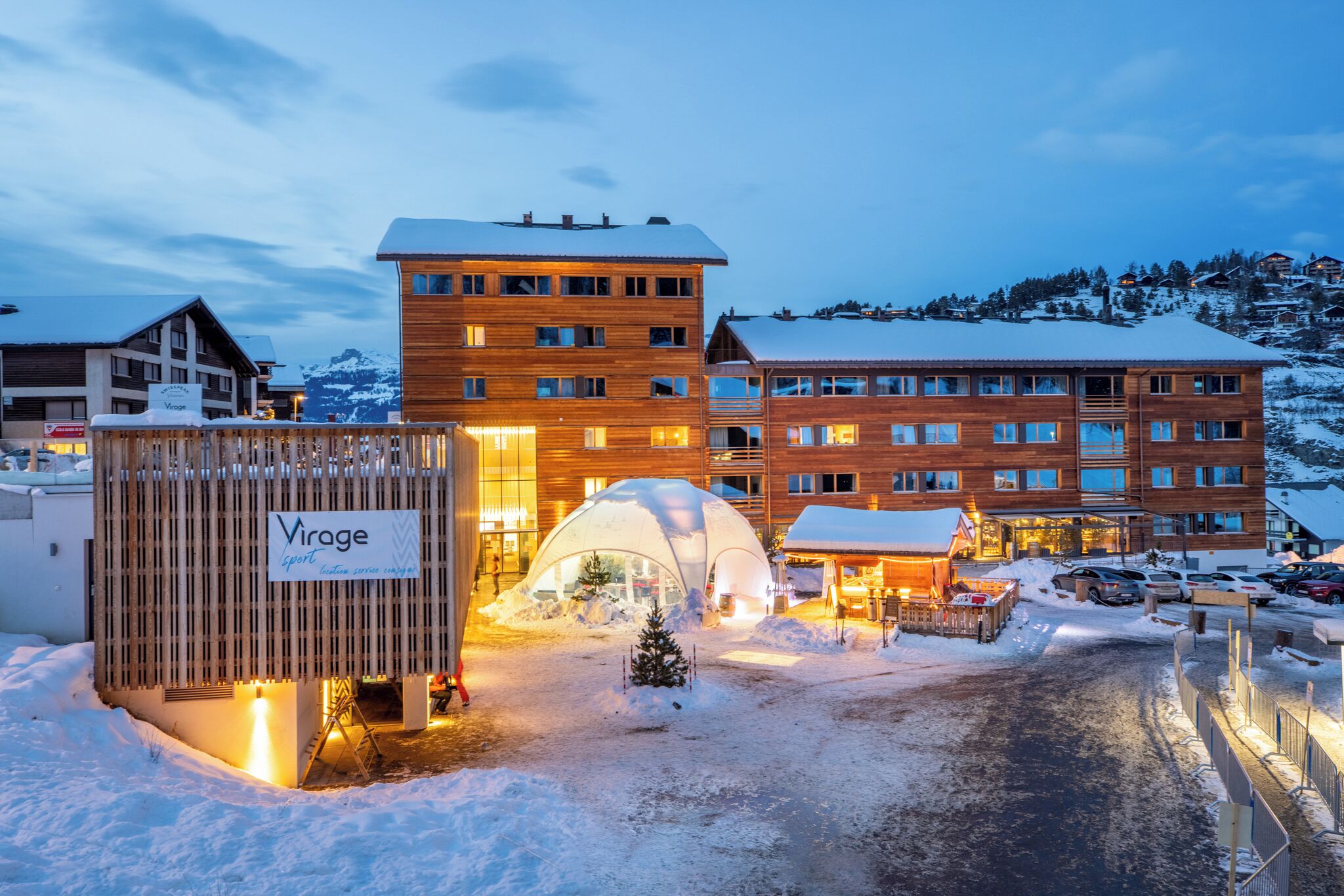 A hotel with a wooden facade, a covered outdoor seating area, and a snow-covered landscape.