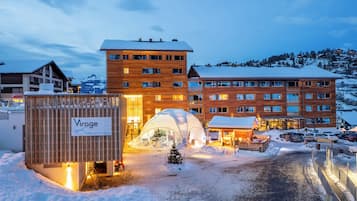 Ein Hotel mit Holzfassade, einer überdachten Außenbestuhlung und verschneiter Landschaft.