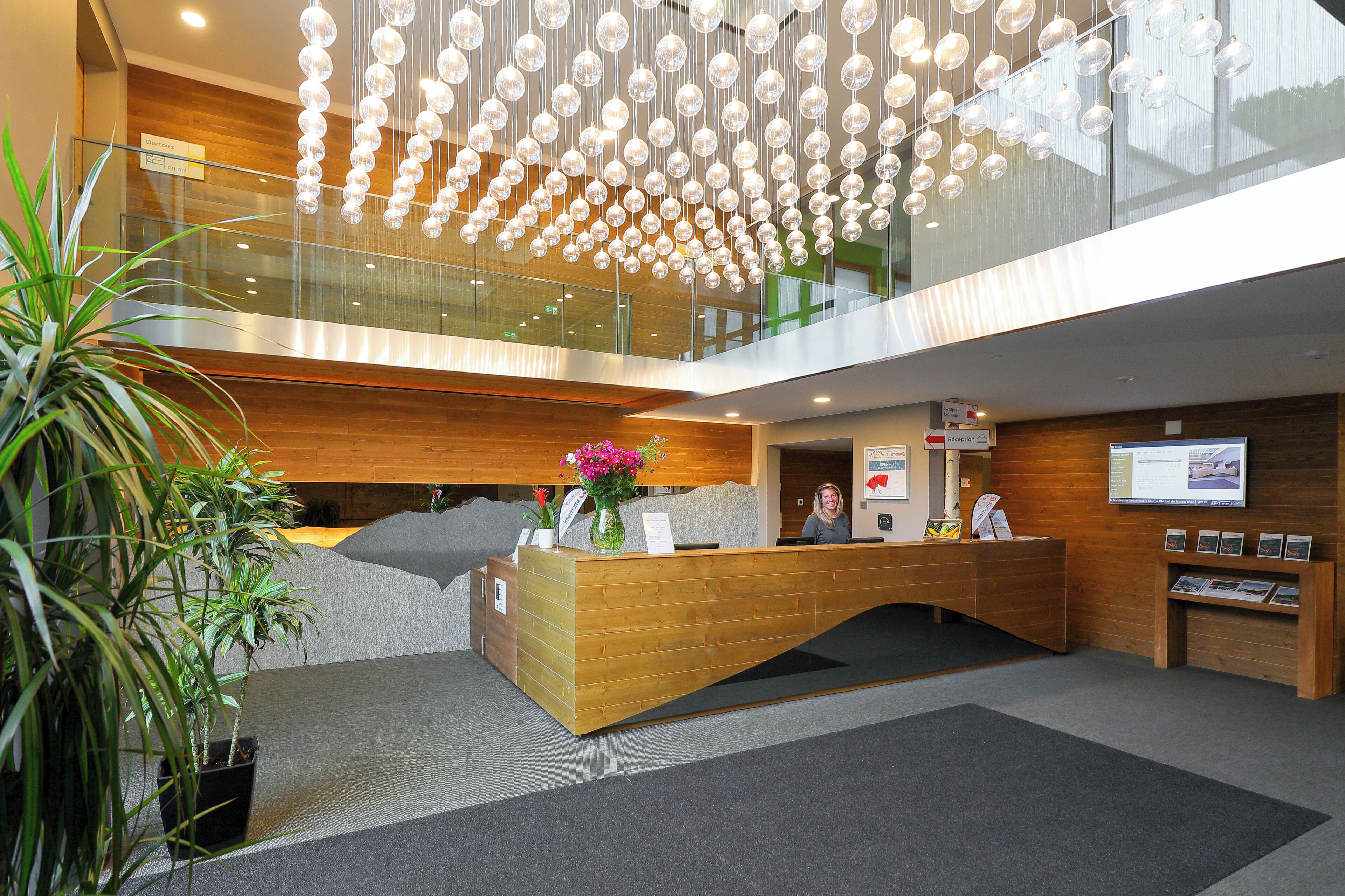 A modern reception desk with a wooden finish, a glass railing, and a hanging light fixture.