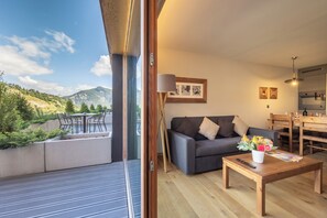 A living room with a sofa, a coffee table, and a dining area with chairs and a table. - SWISSPEAK Resorts by Pierre & Vacances Premium Vercorin (Chalais)