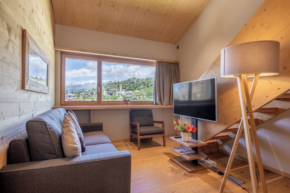 Una habitación acogedora con sofá, sillón, televisor y ventana con vistas a un pueblo.