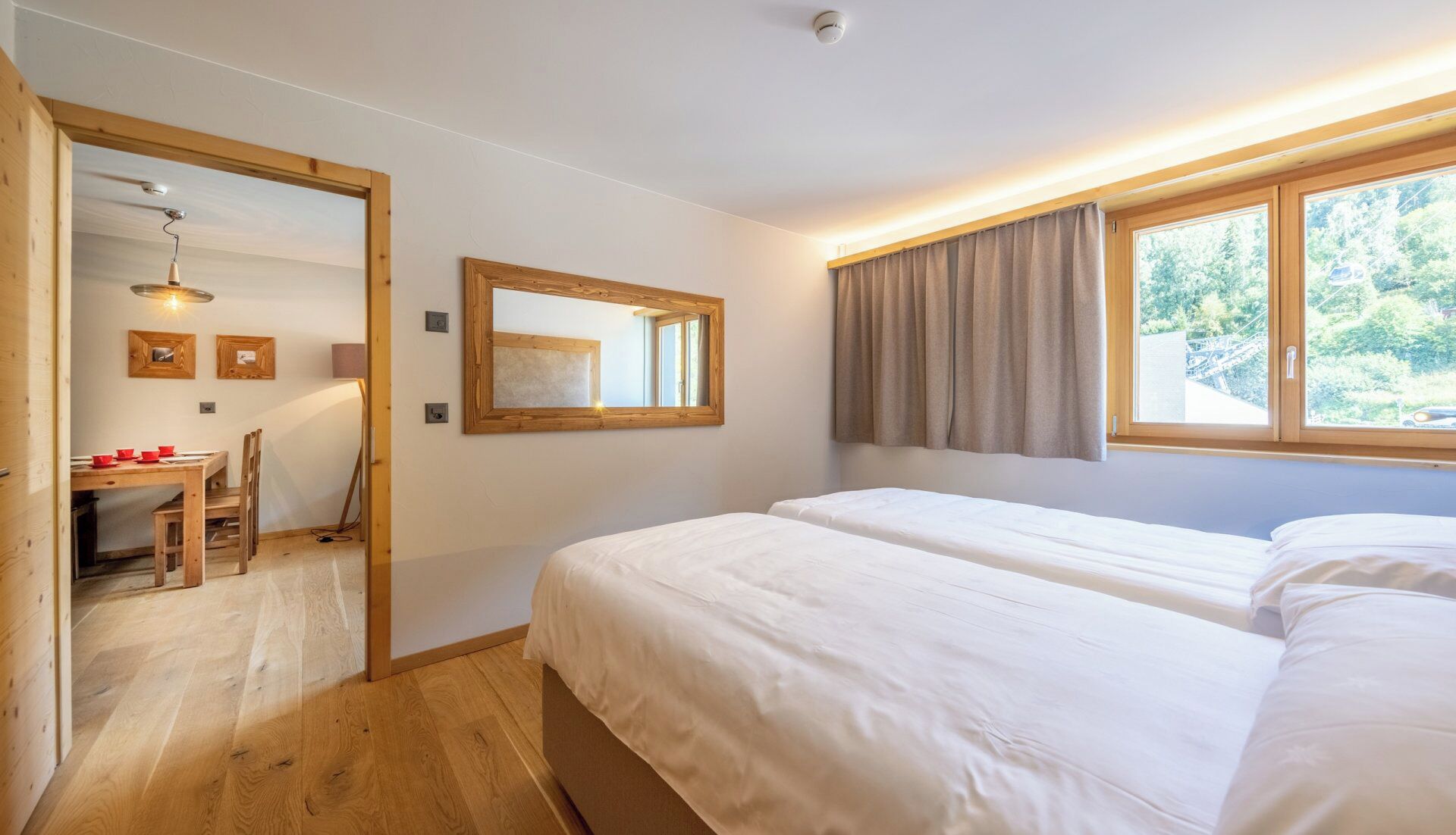 Une chambre avec deux lits, un bureau en bois avec des chaises, un miroir et une fenêtre avec des rideaux.