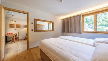 Une chambre avec deux lits, un bureau en bois avec des chaises, un miroir et une fenêtre avec des rideaux.