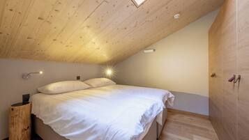 A bedroom with a sloped ceiling, a bed with white bedding, a bedside lamp, and a wardrobe.