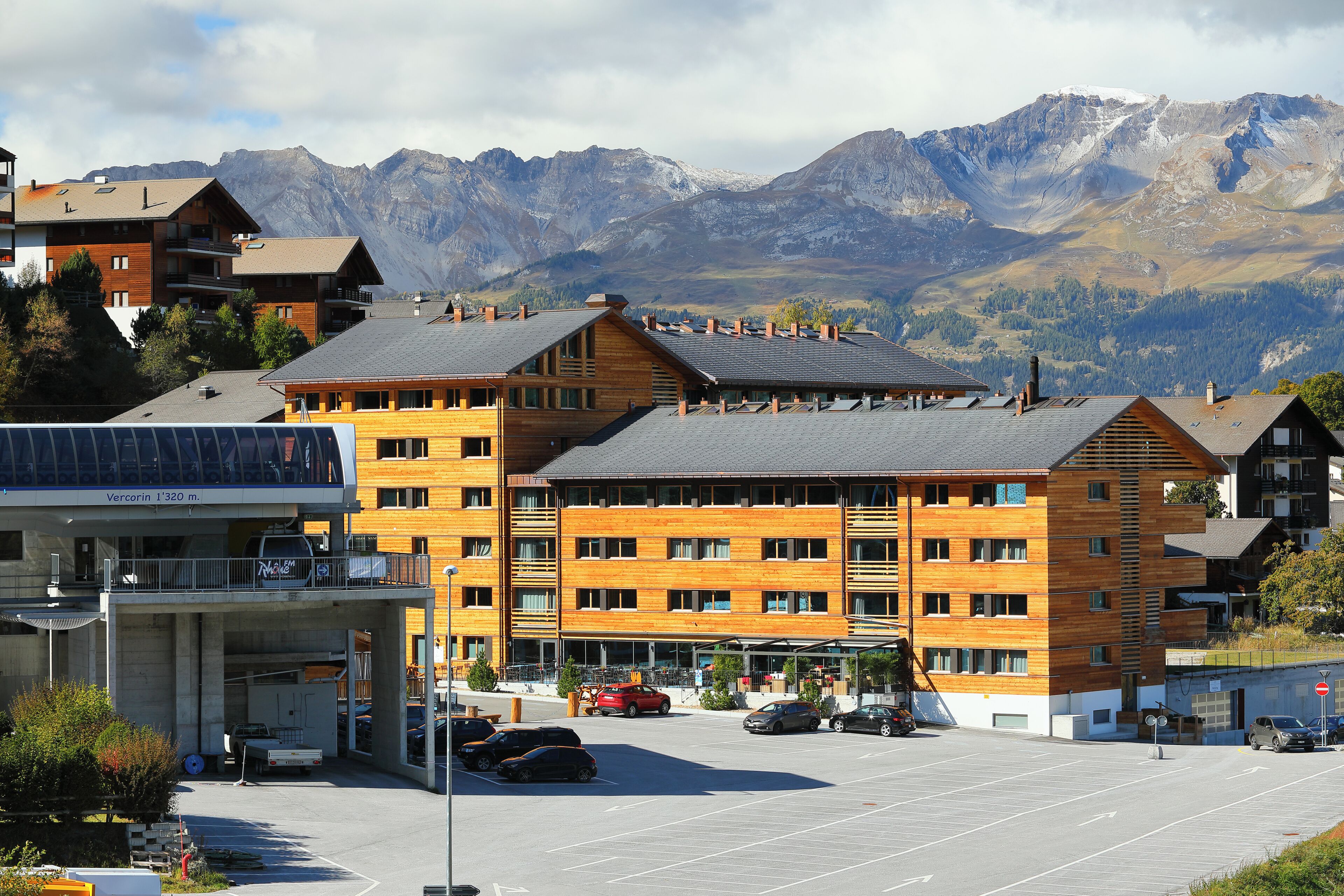 A multi-story hotel with a parking lot, surrounded by mountains.