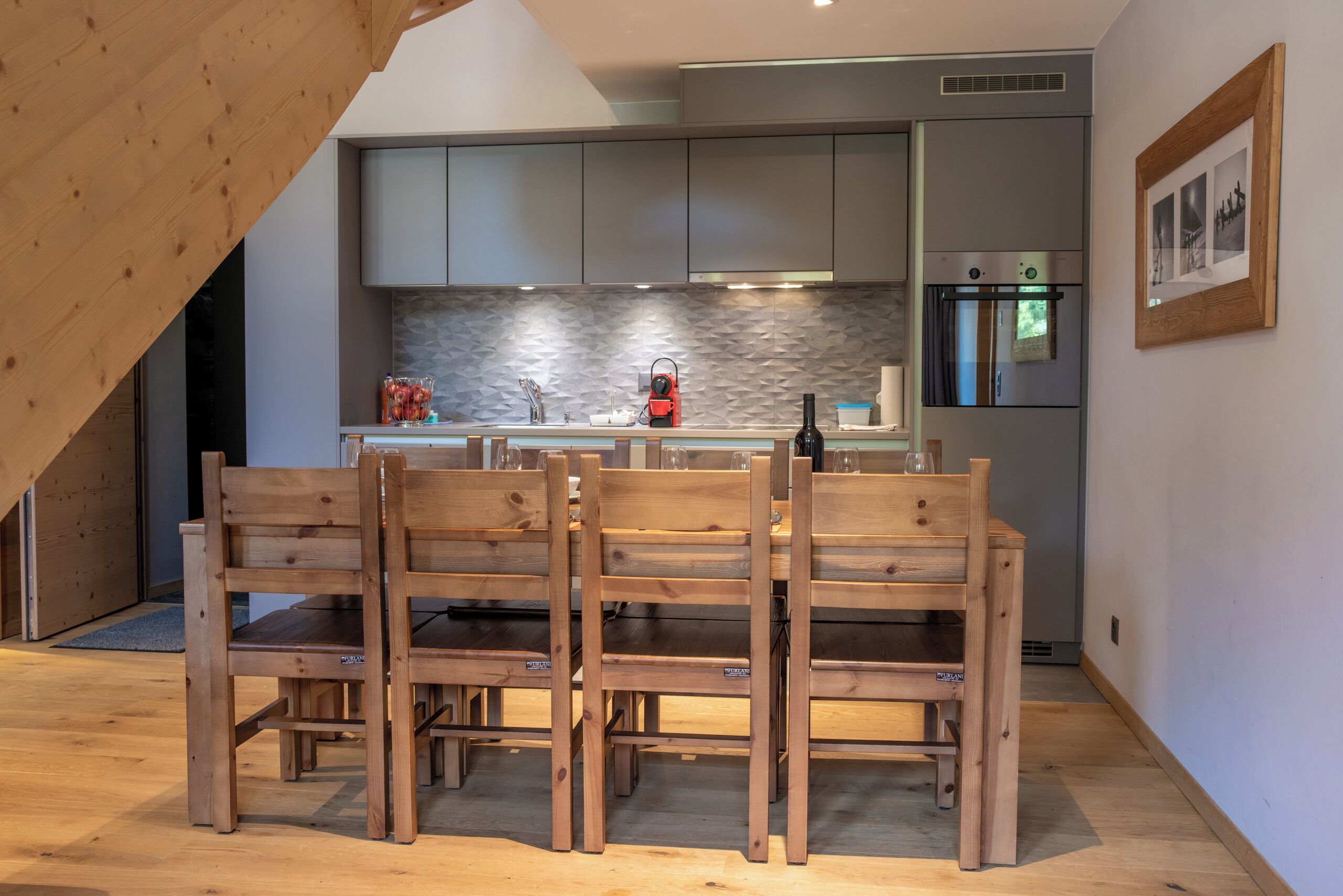 A modern kitchen with wooden chairs, a built-in oven, and a stone backsplash.