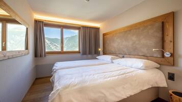 Un dormitorio con dos camas, un ventanal con cortinas, cabecero de madera y vistas a montañas.