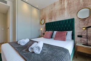 A neatly made bed with rolled towels, a tufted headboard, and a textured wall.