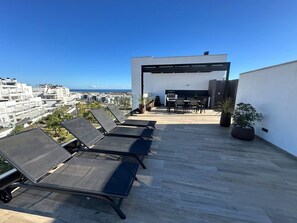 Una terraza en la azotea con sillones de sol, un espacio de descanso y vistas a la ciudad.