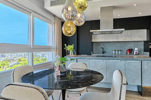 A modern kitchen with a large island, a dining area with a glass table, and a view of the city through large windows.