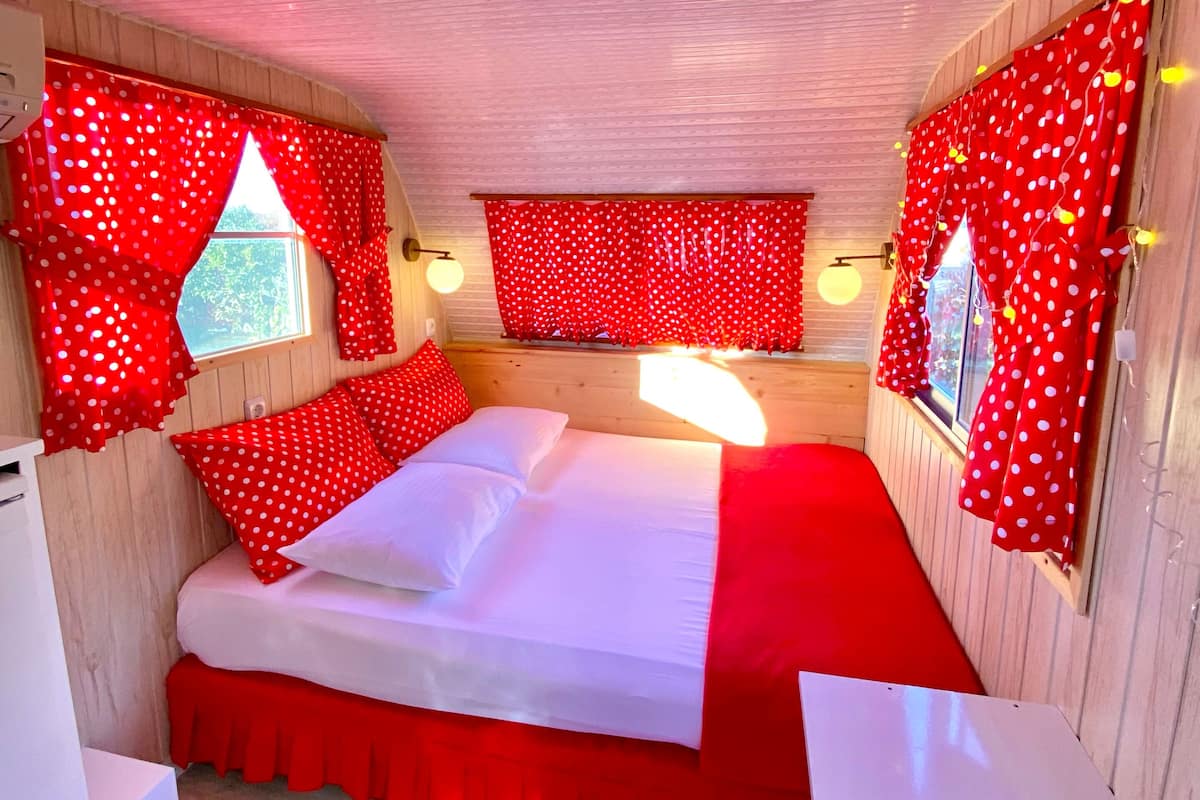 A room with a bed, a small table, and a window with red curtains.