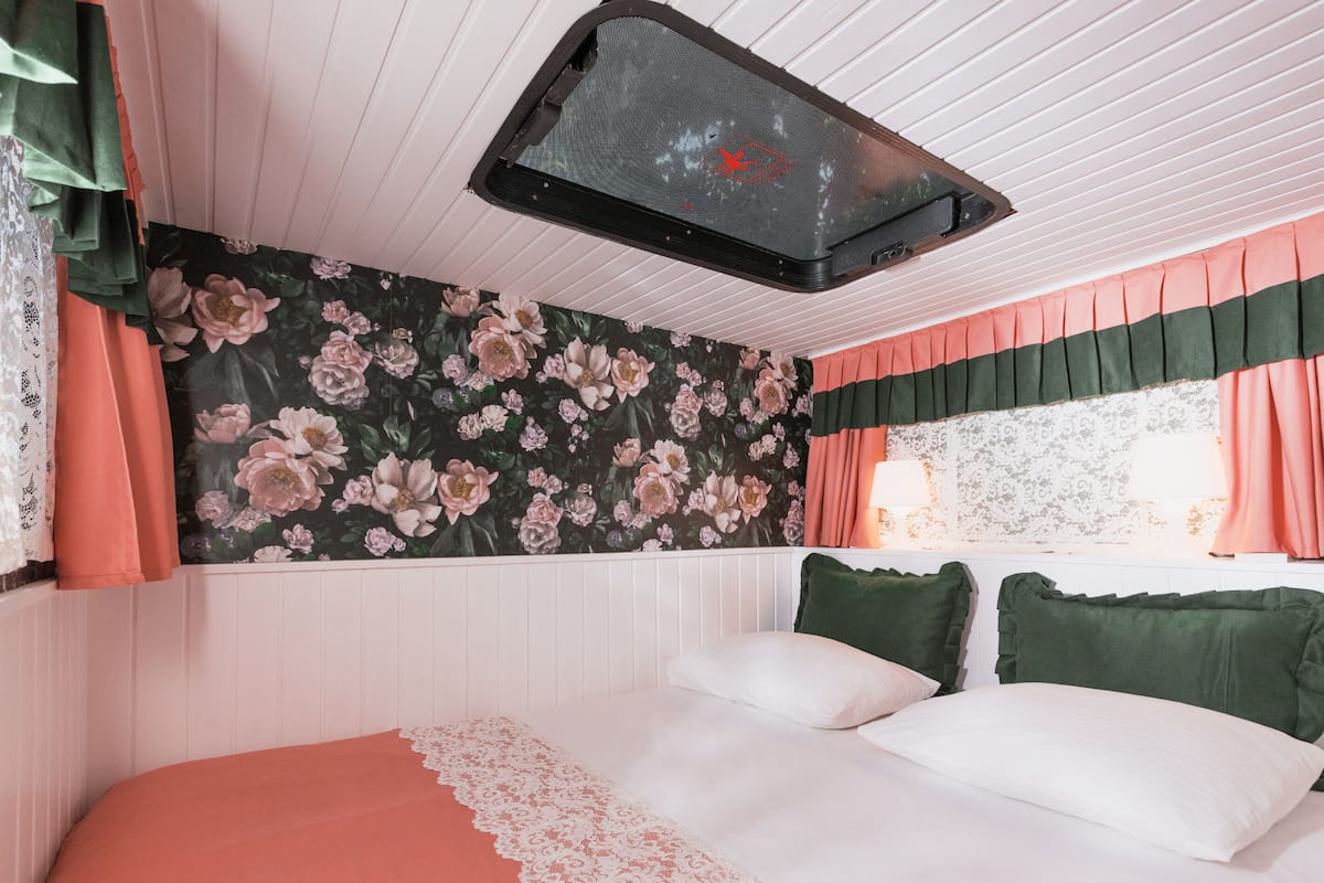 A bedroom with a floral wallpaper, a bed with green and white pillows, and a window with curtains.