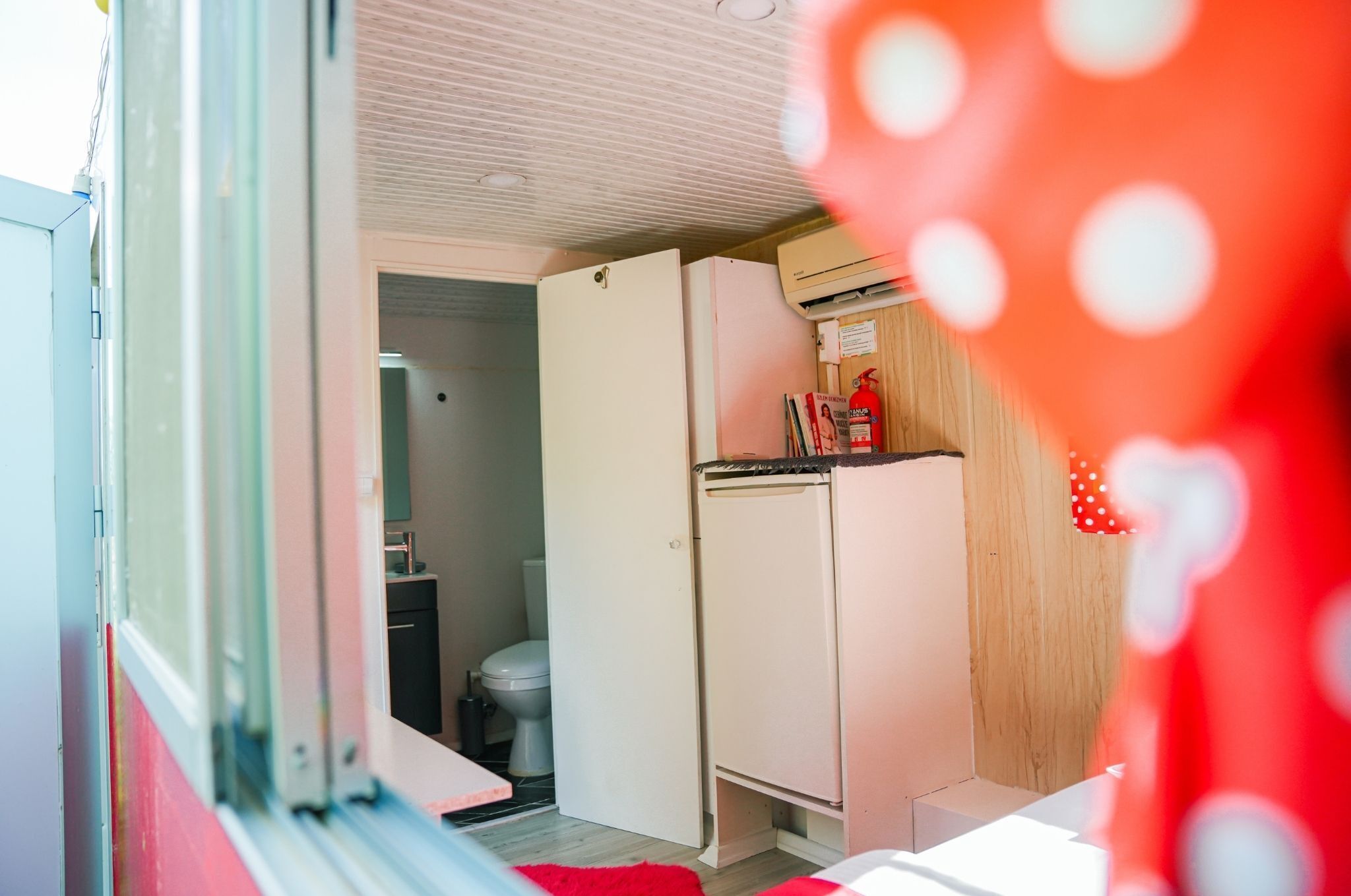 A compact room with a kitchenette, a toilet, and a door leading to another room.