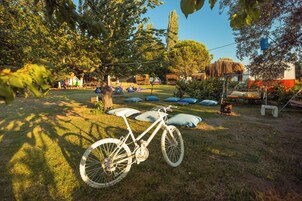 Una bicicleta estacionada en un césped con árboles y una estructura de techo de paja al fondo.