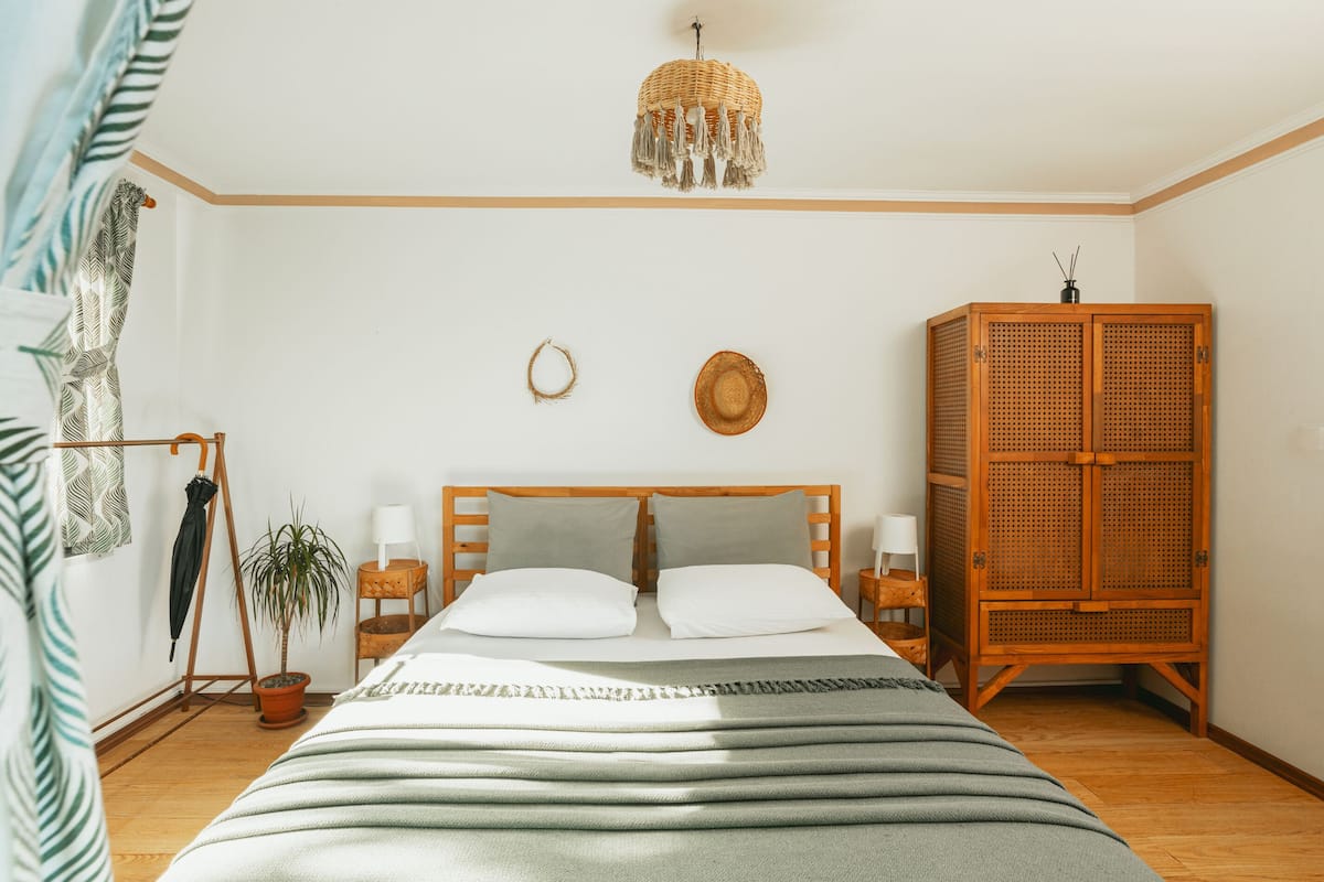 A bedroom with a bed, a wooden wardrobe, a hanging light fixture, and a potted plant.