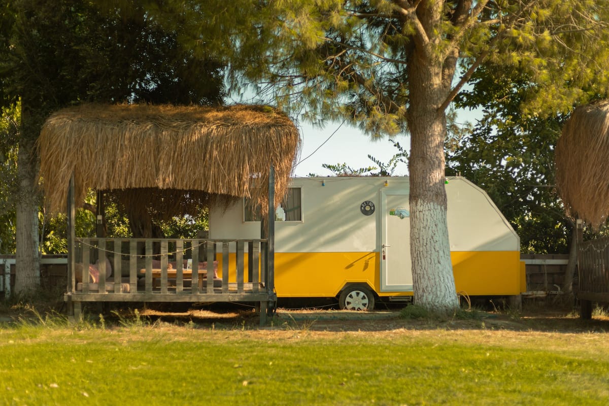 A recreational vehicle (RV) parked in a grassy area with a thatched structure nearby.