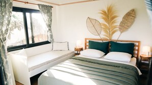 Quarto com cama, um chaise-longue, janela com cortinas, mesa de cabeceira com abajur e grama de pampa decorativa na parede.
