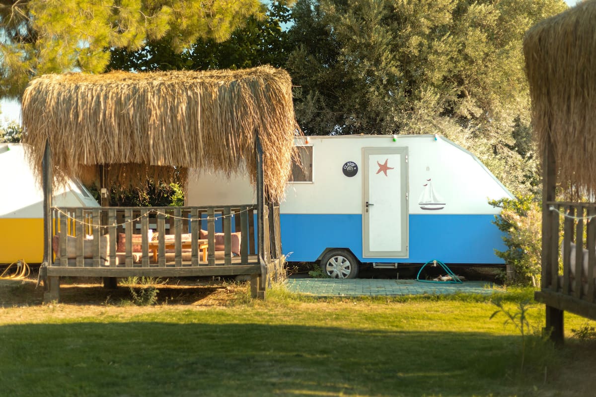 A camper with a thatched roof, a small deck, and a blue and white exterior.