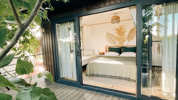 Quarto com cama, mesa de cabeceira e uma janela grande.
