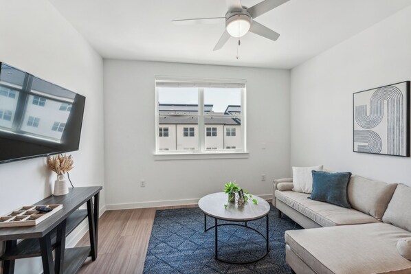 A modern living room with a flat-screen TV, a ceiling fan, a large window, a sofa, and a coffee table. - Spectra Parks 7310, Stunning Austin Oasis (Austin)