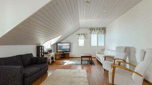 A modern loft apartment with a sloped ceiling, wooden floors, a gray sofa, a white sofa, a wooden chair, a TV, and a bookshelf. - Vacation home Kaisla by Interhome (Joensuu)