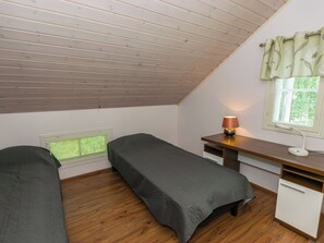 Una habitación pequeña y acogedora con techo inclinado, dos camas individuales, un escritorio con lámpara y una ventana con cortinas.