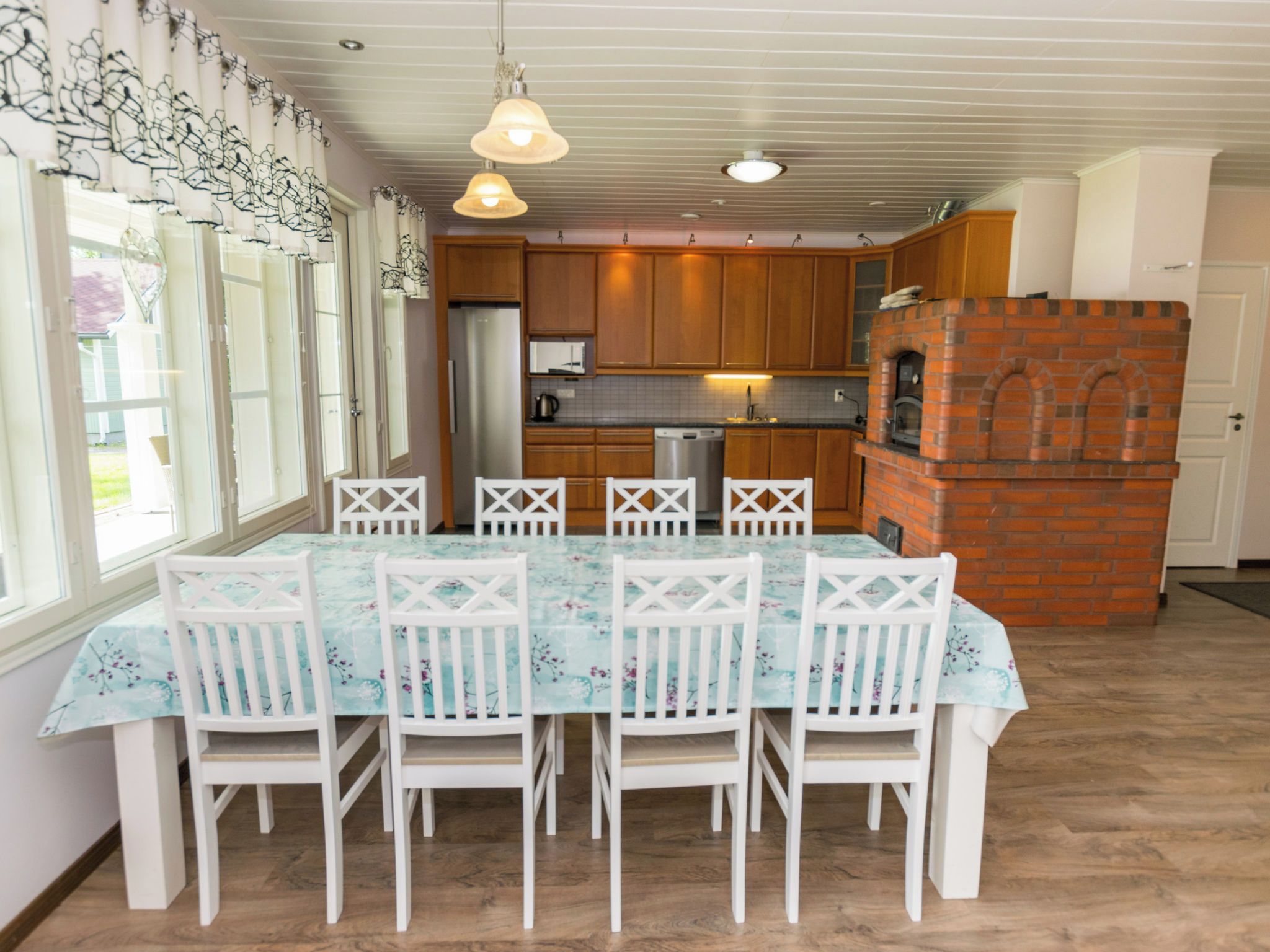 A dining area with a table and chairs, a kitchen with wooden cabinets and a brick oven, and a ceiling with exposed beams.