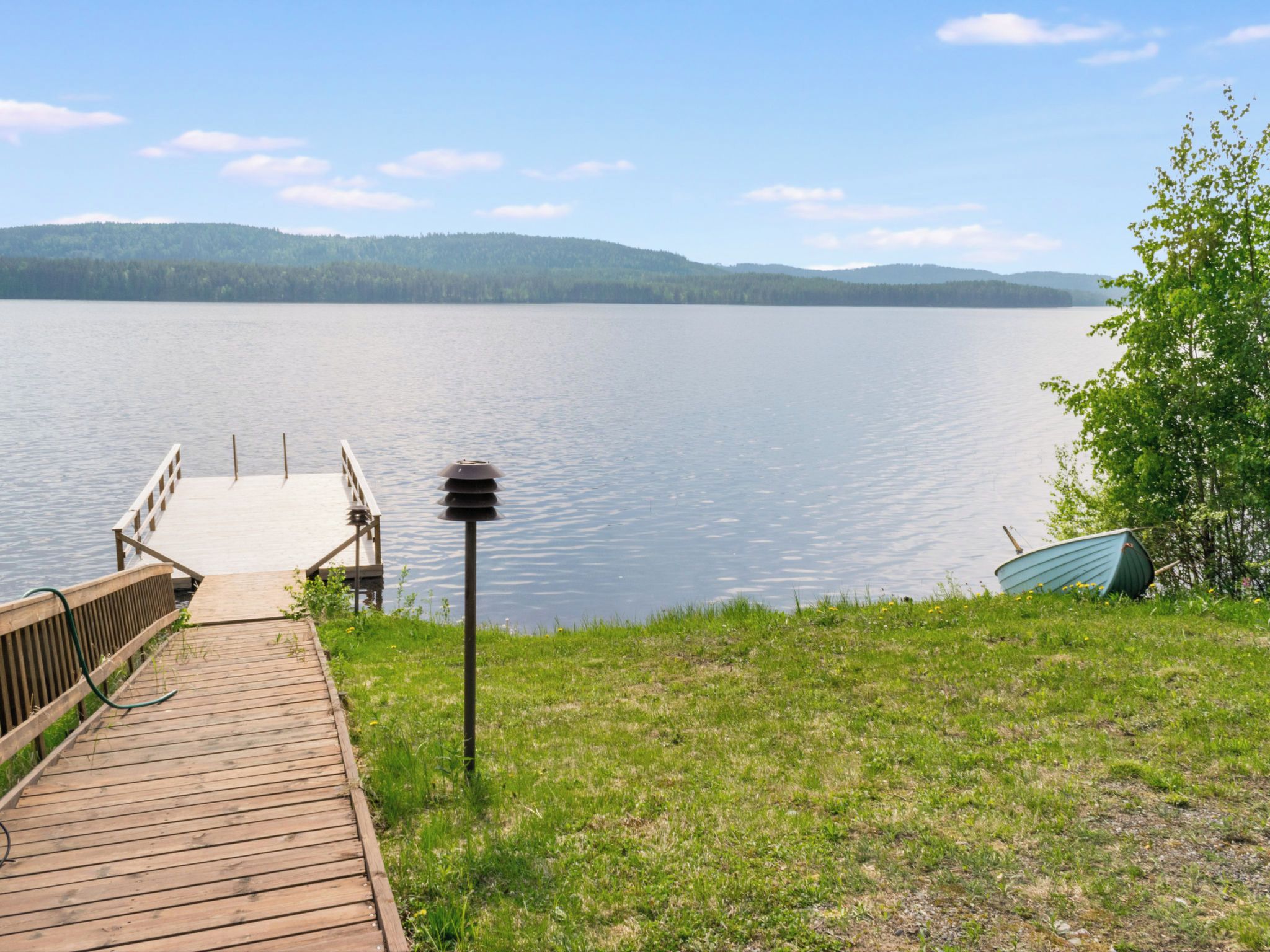 A wooden dock leading to a calm lake with a clear sky and distant hills.