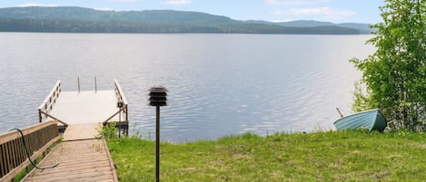 A wooden dock leading to a calm lake with a clear sky and distant hills.