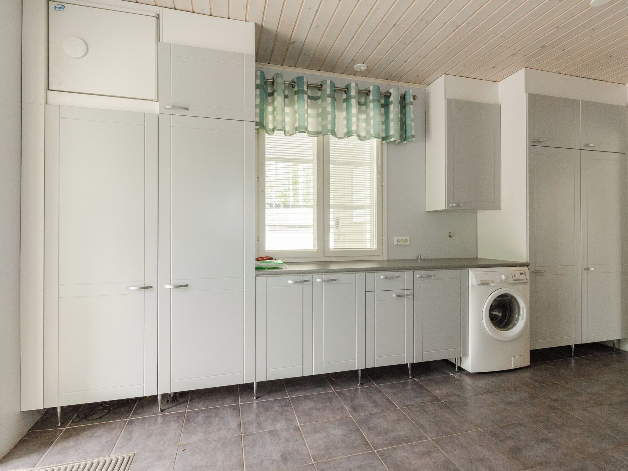 A laundry room with a washing machine, cabinets, and a window with blinds.