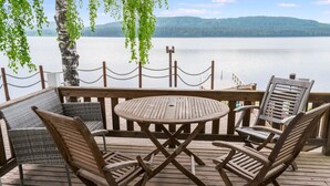 A wooden deck with a round table and four chairs, overlooking a calm lake with distant hills. - Vacation home Kaisla by Interhome (Joensuu)