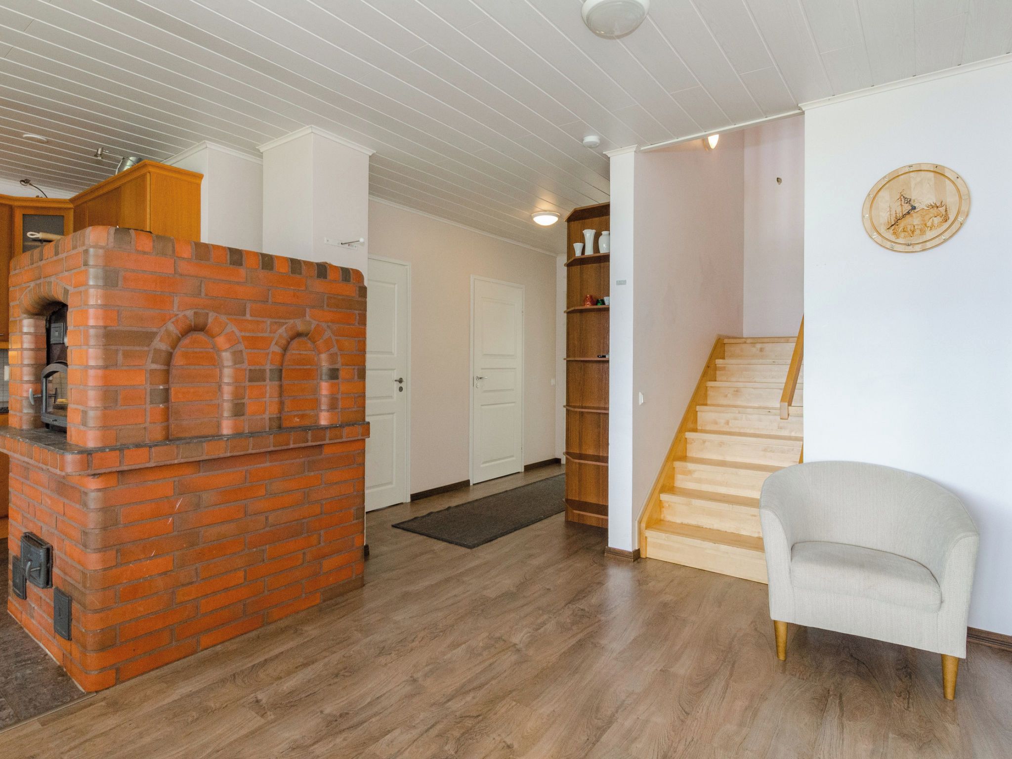Une pièce avec une cheminée en briques, un escalier en bois et un fauteuil.