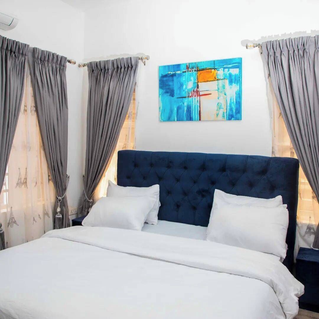 A bedroom with a large bed, grey curtains, and a blue headboard.