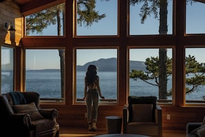 A cabin with large windows offering a view of a body of water and mountains.