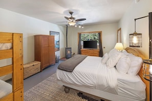 A bedroom with a bed, wooden wardrobe, television, and a ceiling fan.