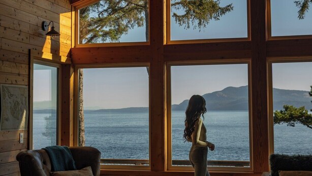 A cabin with large windows, a ceiling fan, and a view of a lake. - Waterfront Retreat w/ Sauna | Whales & Sunrises (Friday Harbor)