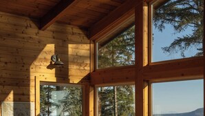 A cozy cabin interior with large windows, a wooden ceiling, and a view of a lake and trees. - Waterfront Retreat w/ Sauna | Whales & Sunrises (Friday Harbor)