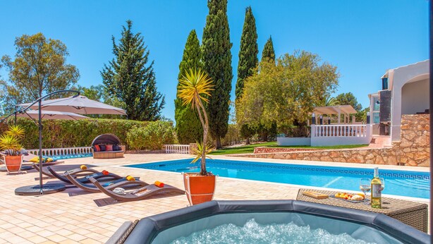 A pool area with lounge chairs, a hot tub, and a stone wall. - Villa Haven (Lagoa)