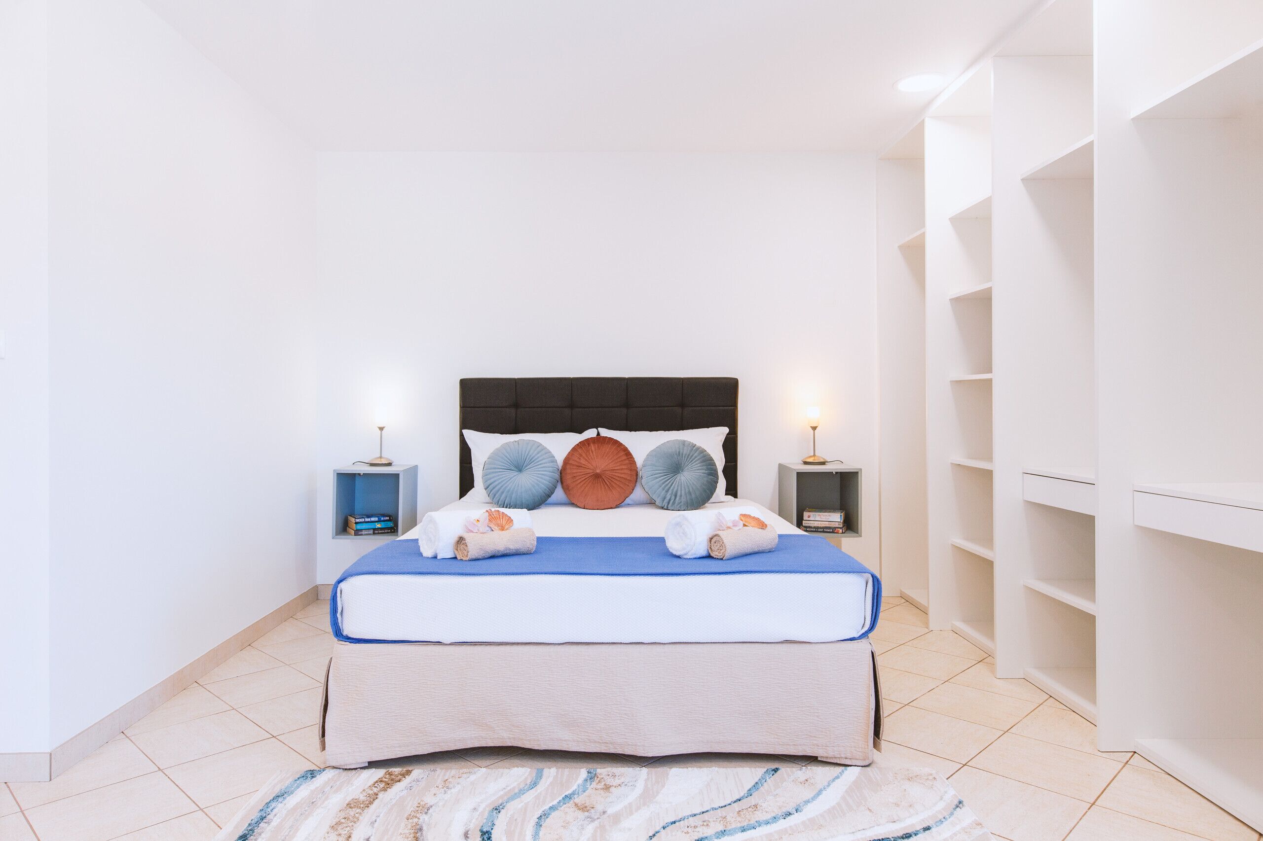 Un dormitorio ordenado con una cama, dos mesitas de noche y una estantería empotrada.