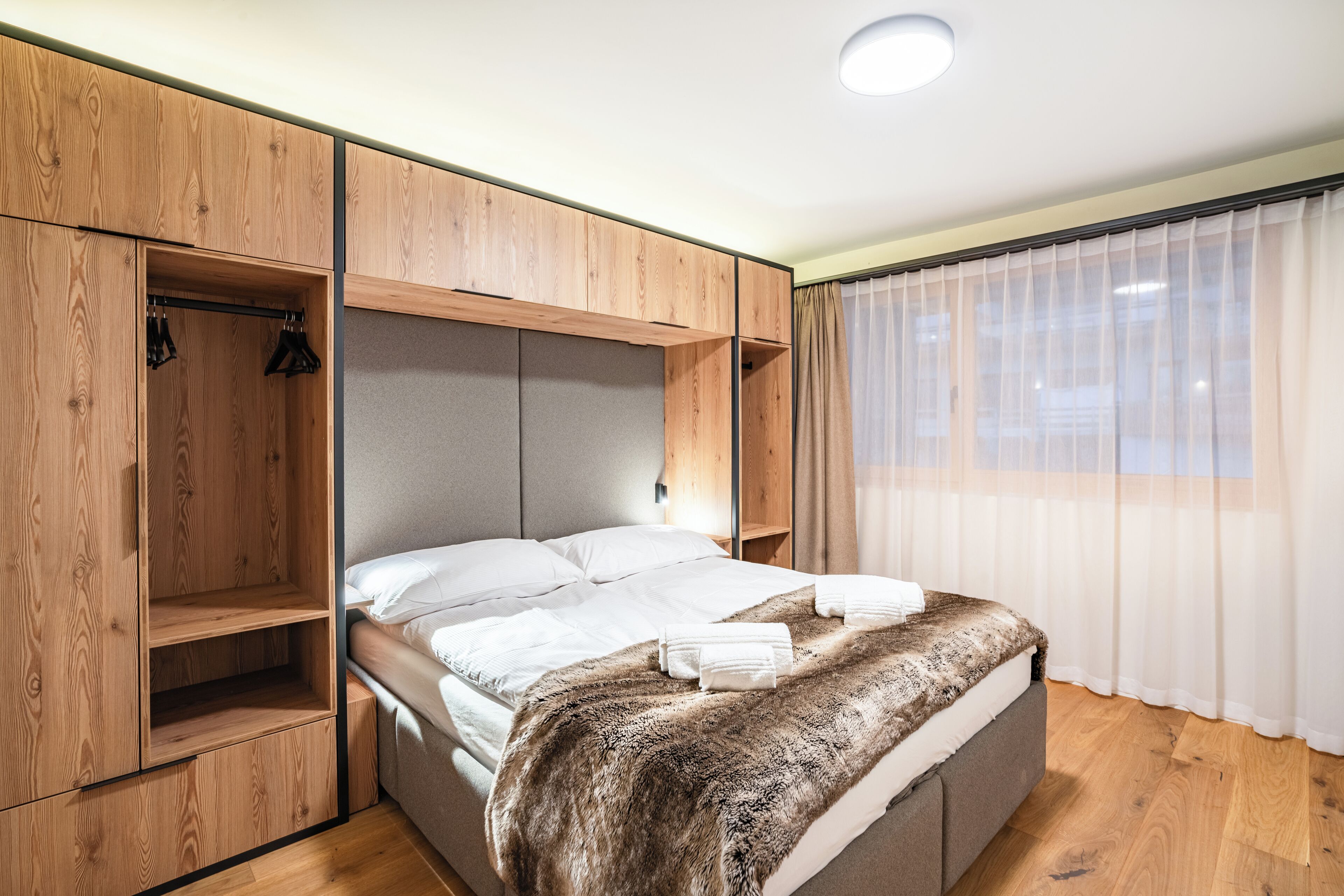 A bedroom with a bed, wooden wardrobe, and a window with curtains.
