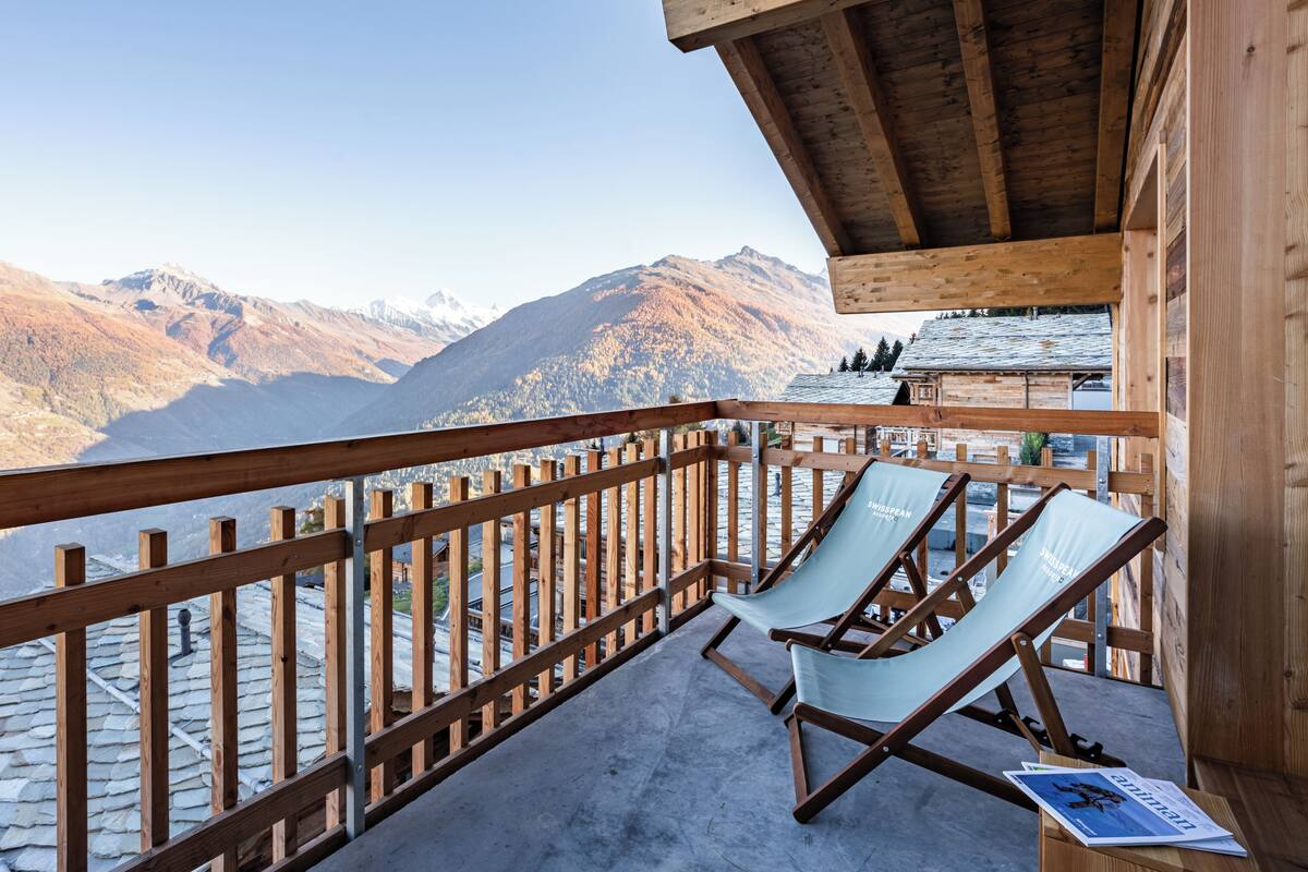 A wooden balcony with two lounge chairs and a view of mountains.