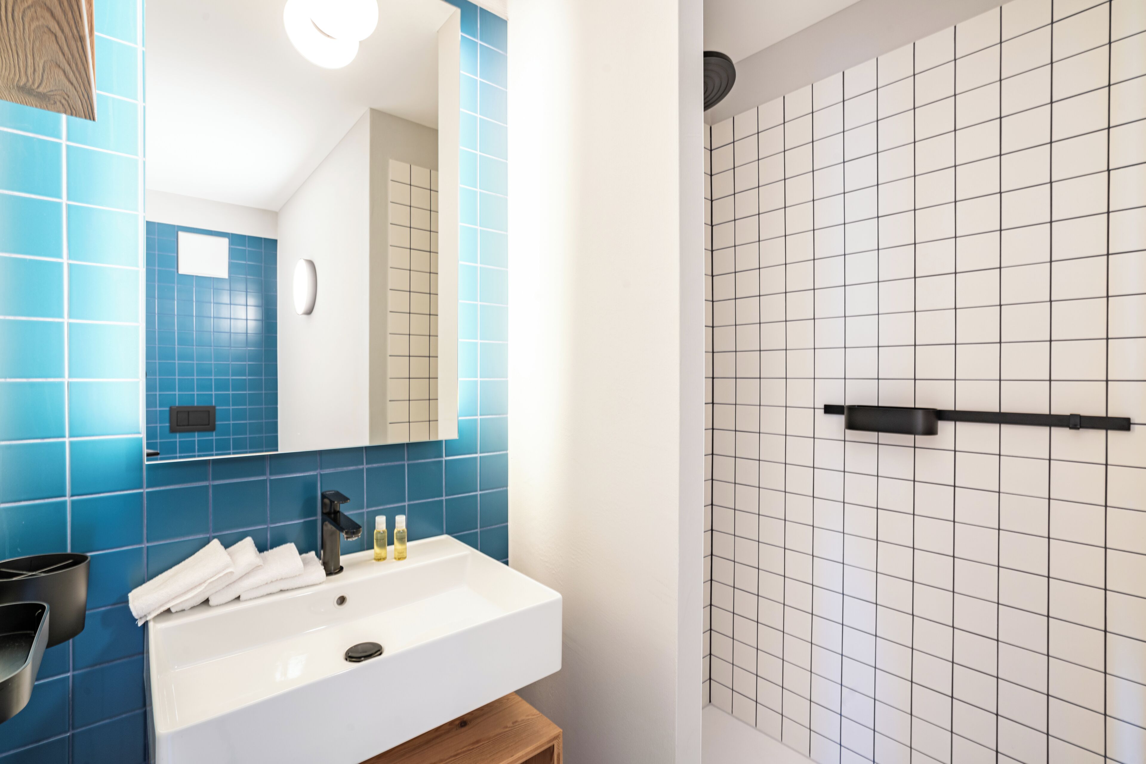 Une salle de bain avec un lavabo blanc, des carreaux bleus, un miroir et un espace douche.