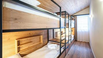 A bunk bed room with wooden headboards, a wooden floor, and a window with curtains.