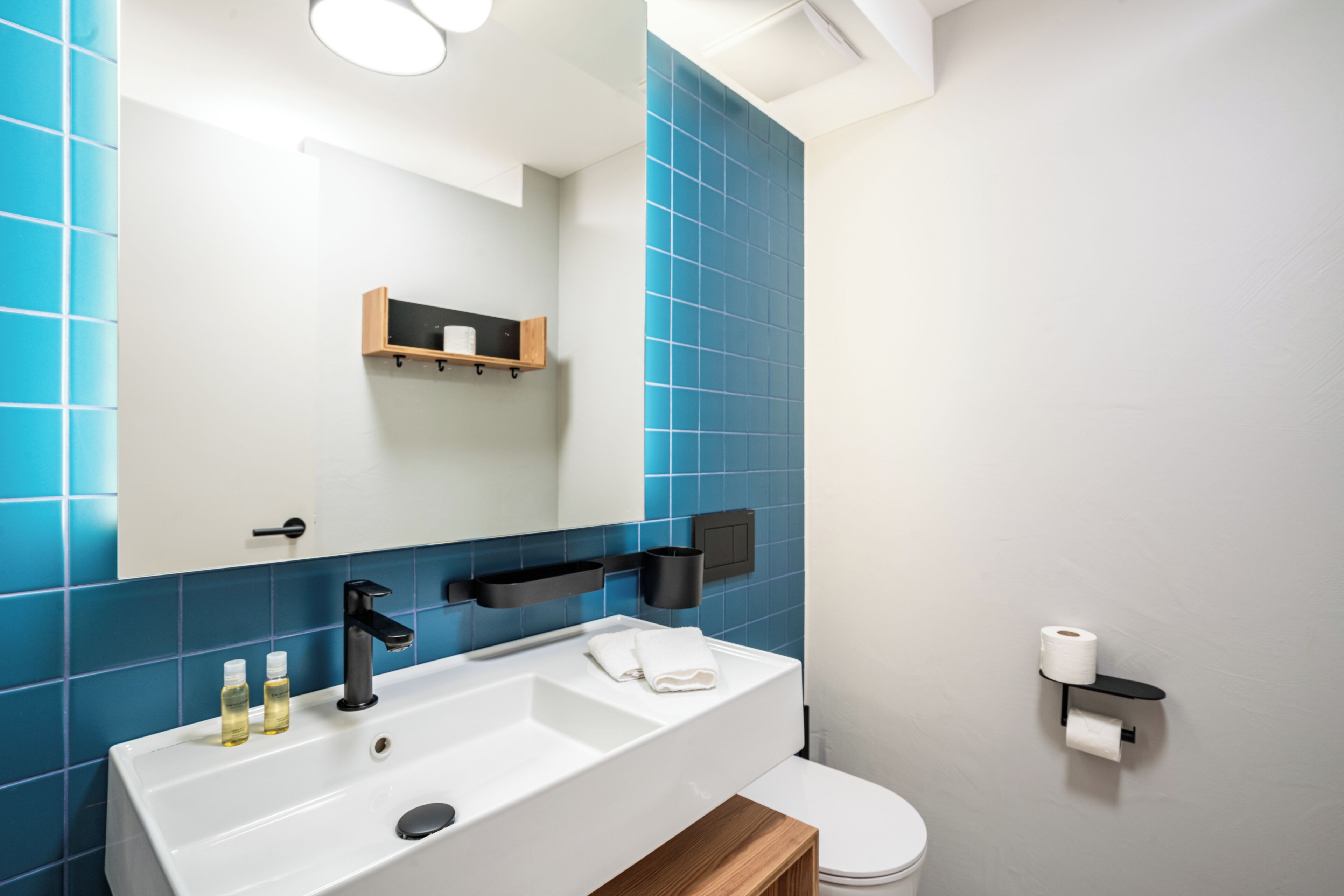 A modern bathroom with a white sink, blue tiles, a mirror, and a toilet.